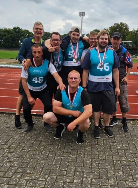Acht Mitglieder des Special Olympics-Team der Pestalozzi-Stiftung posieren vor der Kamera mit ihren Medaillen vor einer Asche-Laufbahn.