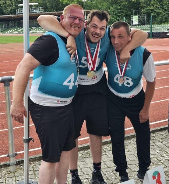 Drei Mitglieder des Special Olympics-Team der Pestalozzi-Stiftung posieren vor der Kamera mit ihren Medaillen vor einer Asche-Laufbahn.