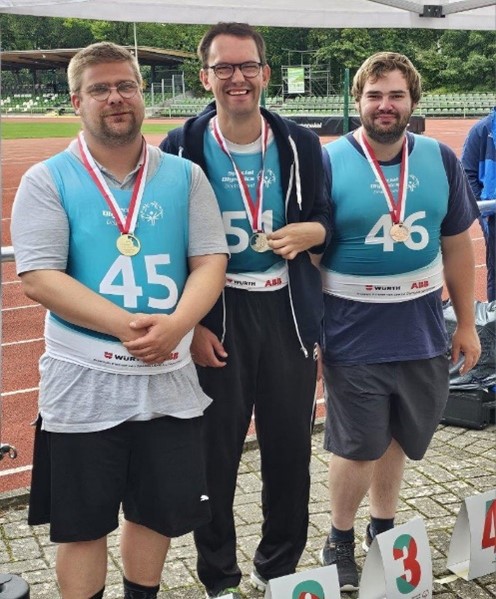 Drei Mitglieder des Special Olympics-Team der Pestalozzi-Stiftung posieren vor der Kamera mit ihren Medaillen vor einer Asche-Laufbahn.