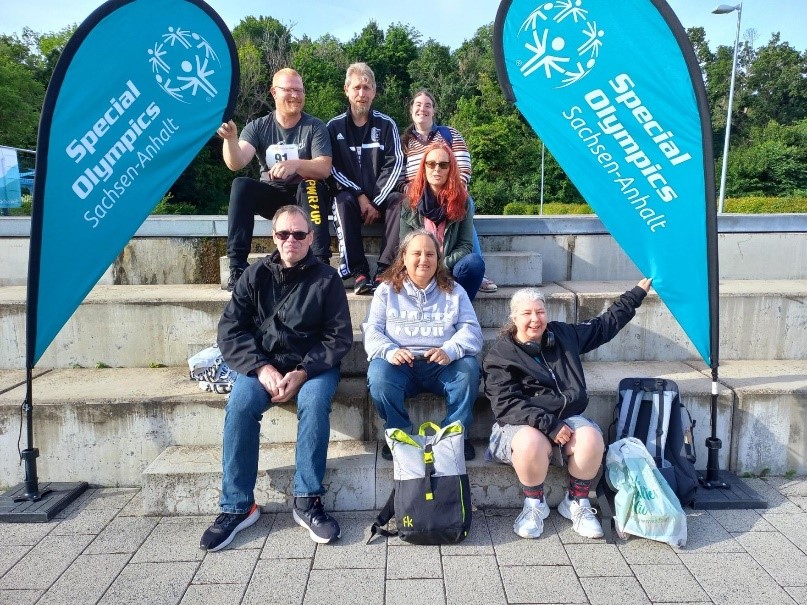 sieben Personen sitzen draußen auf einer Steintreppe, sie gehören zum Special Olympics-Team der Pestalozzi-Stiftung.