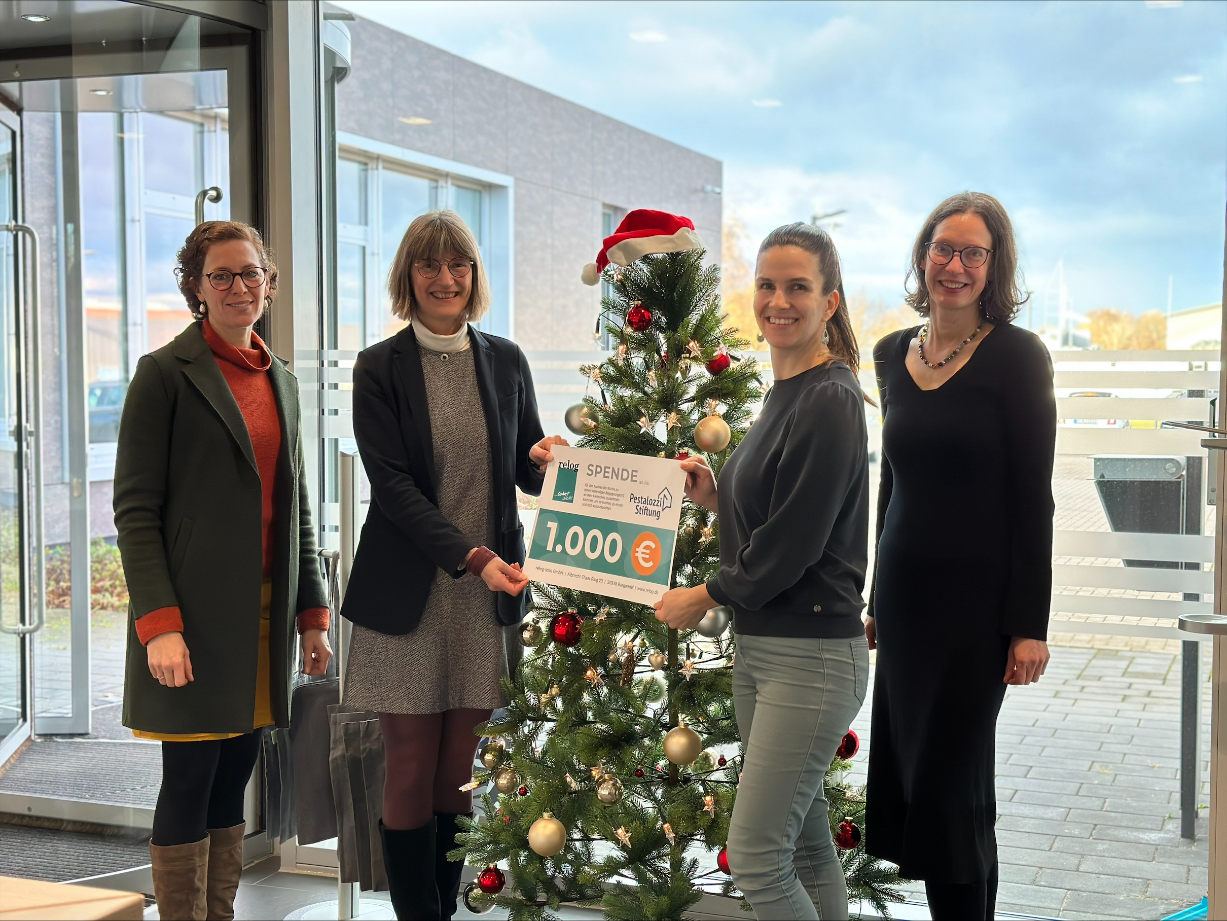 Zu sehen sind 4 Personen vor einem Weihnachtsbaum, die eine Spende über 1000€ überreichen.